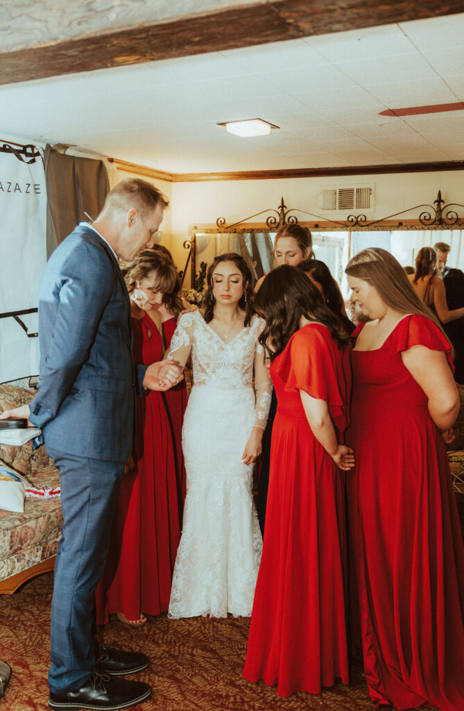 bride getting prayed over by bridesmaid and father