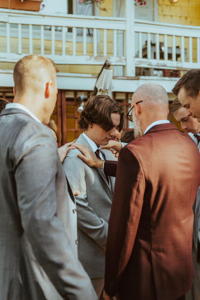 groom getting prayed over by groomsmen and father