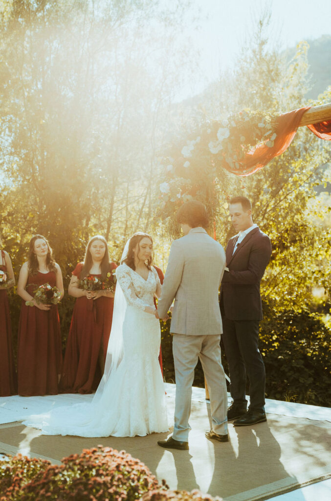 ceremony wedding photo in Oregon while bride and groom share vows as the river breeze is felt. celebrating love surrounded by fall foliage and the beautiful Oregon riverside. A very romantic fall wedding with golden leaves.
