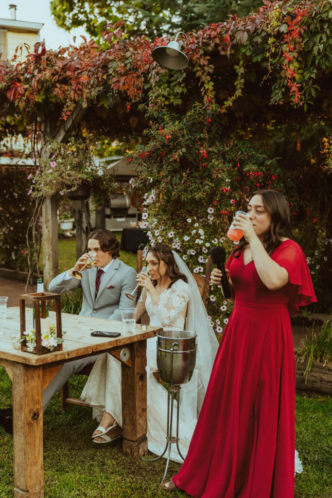 Maid of honor giving speech at wedding with red flowers in the back during fall ;Golden Leaves and River Breeze