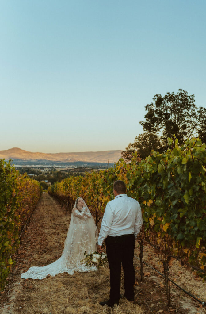 groom looking at bride in the vineyard while holding her flowers