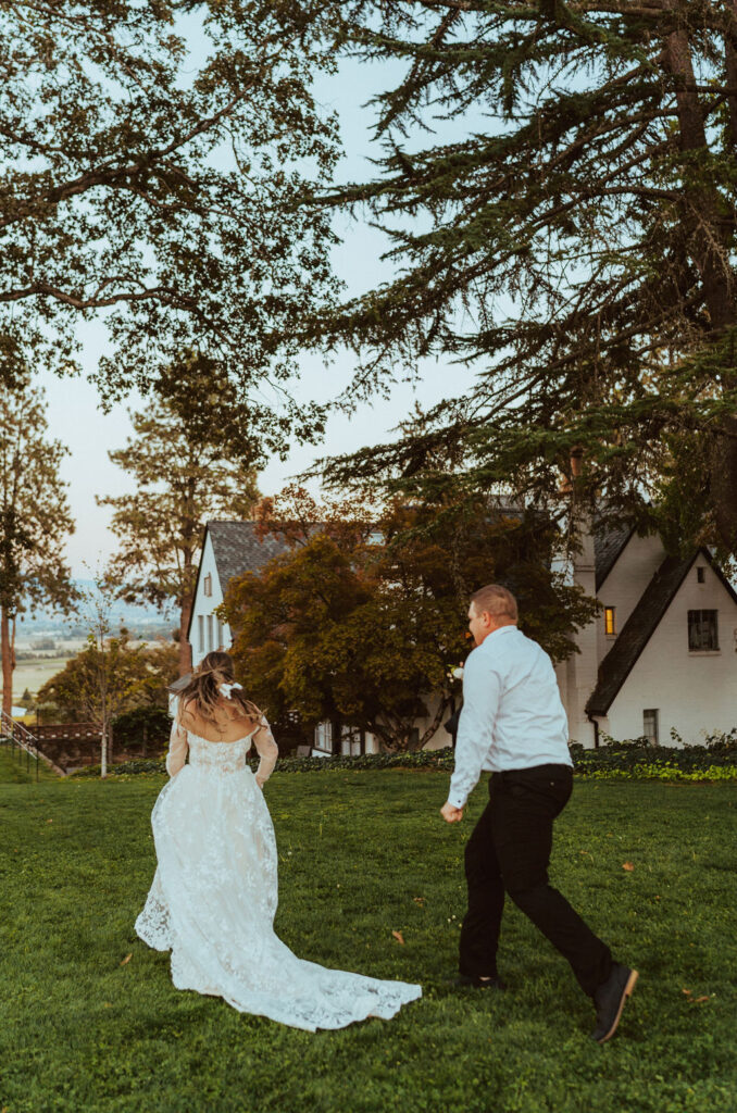 groom chasing bride in the grass in their wedding attire