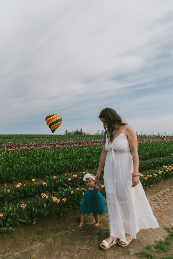 mom and little girl walking in the tulip field with hot air balloon in the background
